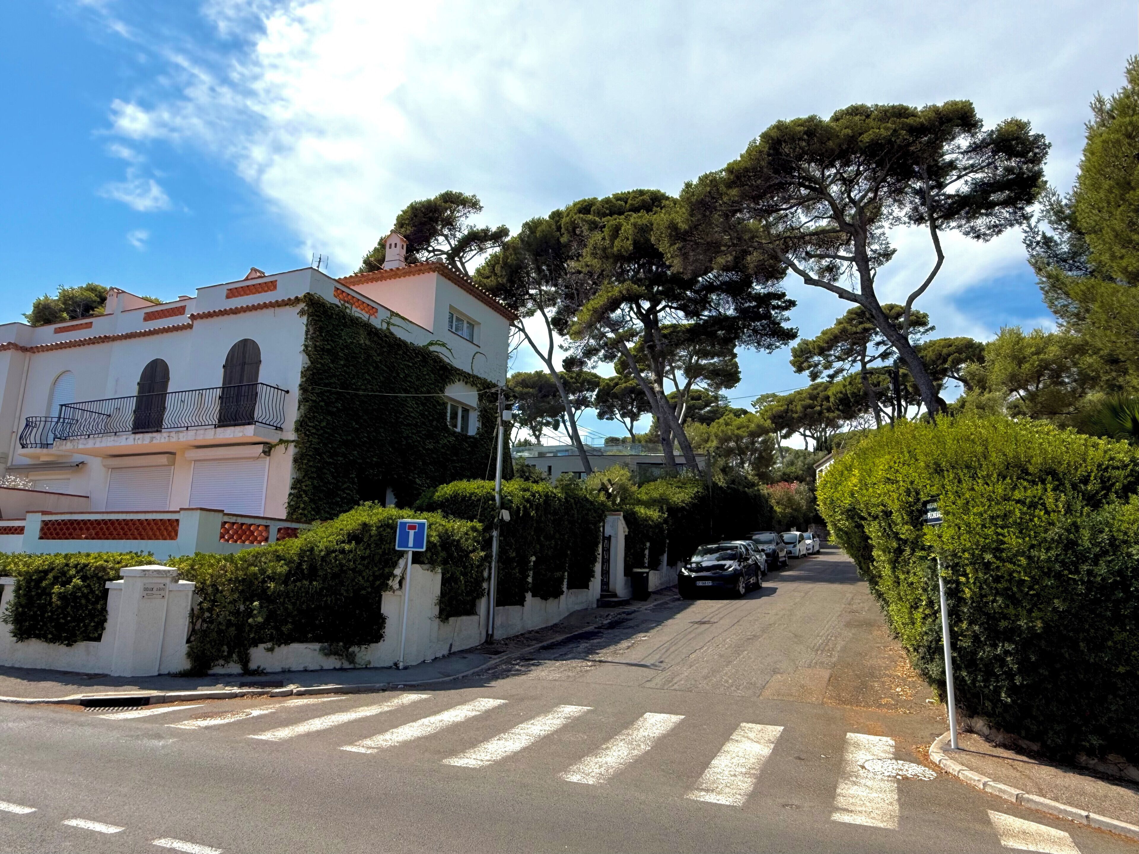 A street with a building featuring a balcony and a row of parked cars.
