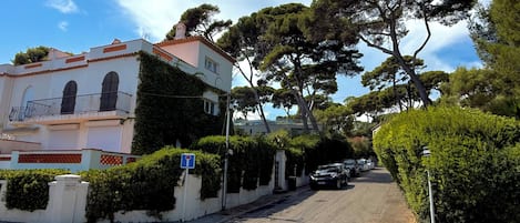 A street with a building featuring a balcony and a row of parked cars.