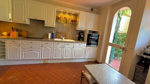 A kitchen with white cabinets, a granite countertop, a built-in oven, and a window with a view of greenery. - Cap d'Antibes, view of La Garoupe beach – Sleeps 8 – Garden and terrace (Antibes)