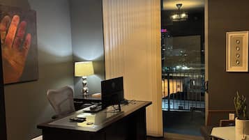 A hotel room with a desk, computer, lamp, and a view of the city through a window.