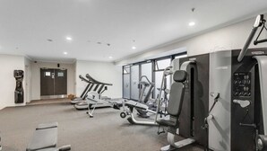 A gym with cardio machines, weight stations, and a wall-mounted exercise bike. - Queen Street Gem - Freshly Renovated Studio (Auckland CBD)