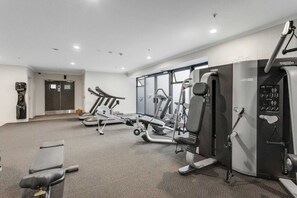 A gym with cardio machines, weight stations, and a wall-mounted exercise bike. - Queen Street Gem - Freshly Renovated Studio (Auckland CBD)