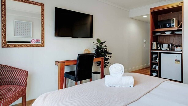 A hotel room with a bed, a desk with a chair, a television, a small kitchenette, and a 'NO Smoking' sign. - Queen Street Gem - Freshly Renovated Studio (Auckland CBD)