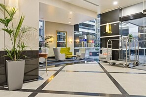 A hotel lobby with a reception desk, seating area, and a view of the outside. - Queen Street Gem - Freshly Renovated Studio (Auckland CBD)