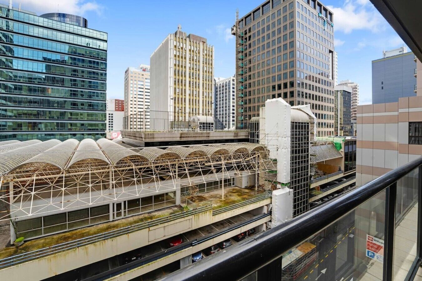A modern building with a unique arched roof structure, surrounded by high-rise buildings.