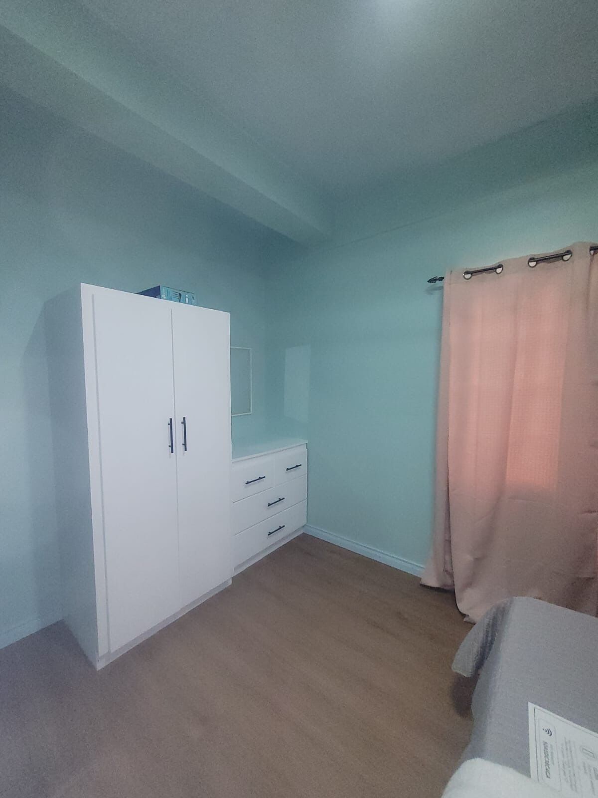 A bedroom with a wardrobe, a bedside table, and a window with curtains.