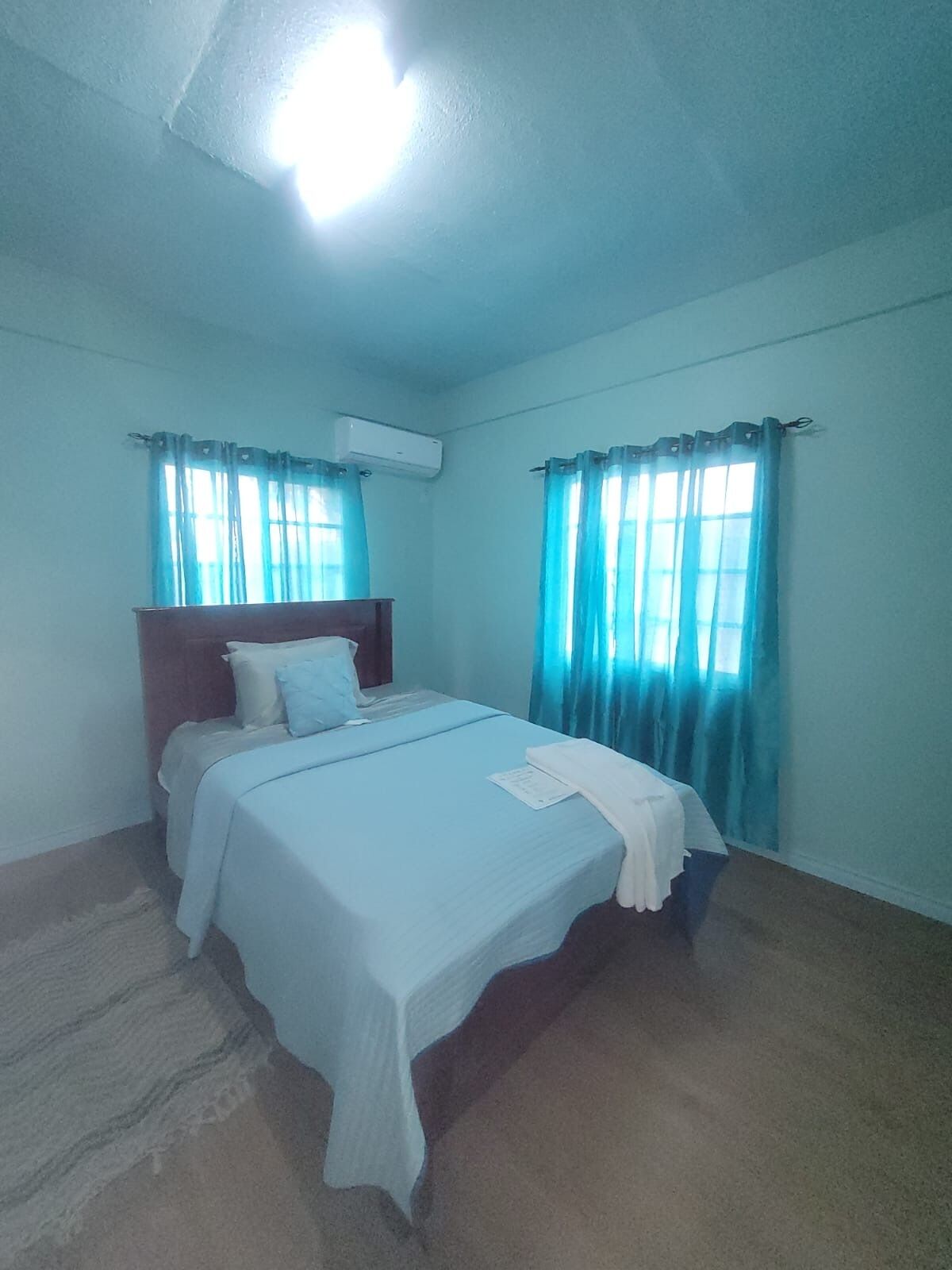 A bedroom with a bed, curtains, an air conditioning unit, and a carpeted floor.