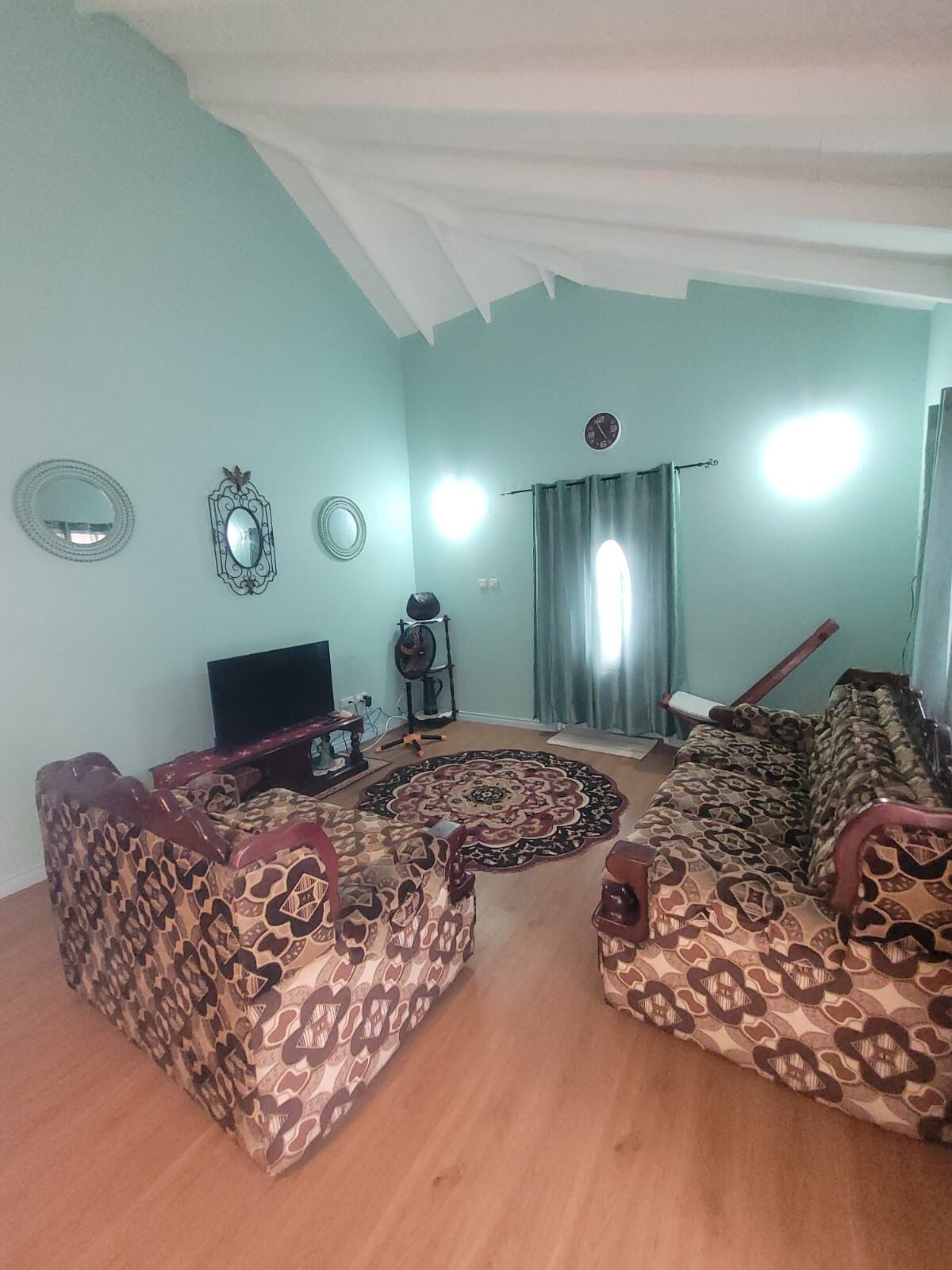 Ein Wohnzimmer mit gemusterten Sofas, einem Fernseher und einem Ventilator.