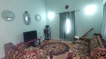 Ein Wohnzimmer mit gemusterten Sofas, einem Fernseher und einem Ventilator.