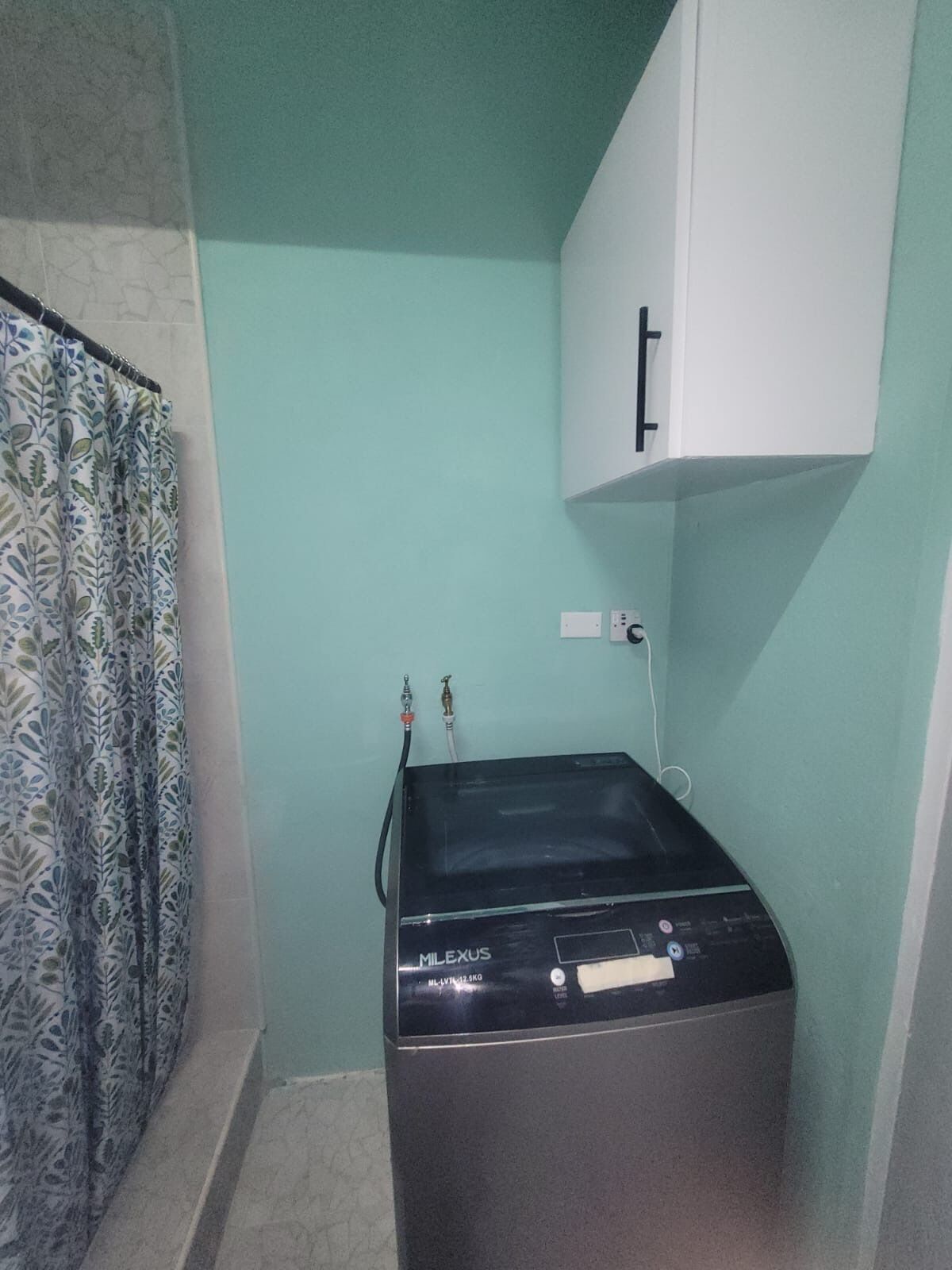 A compact room with a washing machine, a white cabinet, and a patterned curtain.