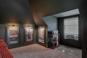 A room with a sloped ceiling, a window, and posters on the wall. - Amber & Oak: Theater, Game Room & Fire Pit (Omaha)