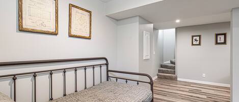 A bedroom with a bed, a framed blueprint on the wall, and a staircase leading to another room.