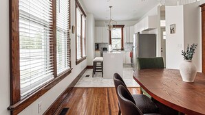 A modern kitchen with a central island, wooden flooring, and a dining area with a table and chairs. - Amber & Oak: Theater, Game Room & Fire Pit (Omaha)