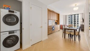 Un apartamento compacto con lavandería, una kitchenette, un comedor con mesa y sillas, y vista a un edificio a través de una ventana.