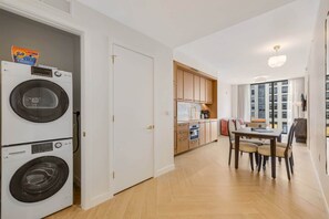 Eine kompakte Wohnung mit Waschbereich, einer Küchenzeile, einer Essecke mit Tisch und Stühlen sowie Blick auf ein Gebäude durch ein Fenster.