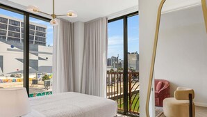 Habitación de hotel con una cama grande, un balcón con vistas a la ciudad y una silla moderna.