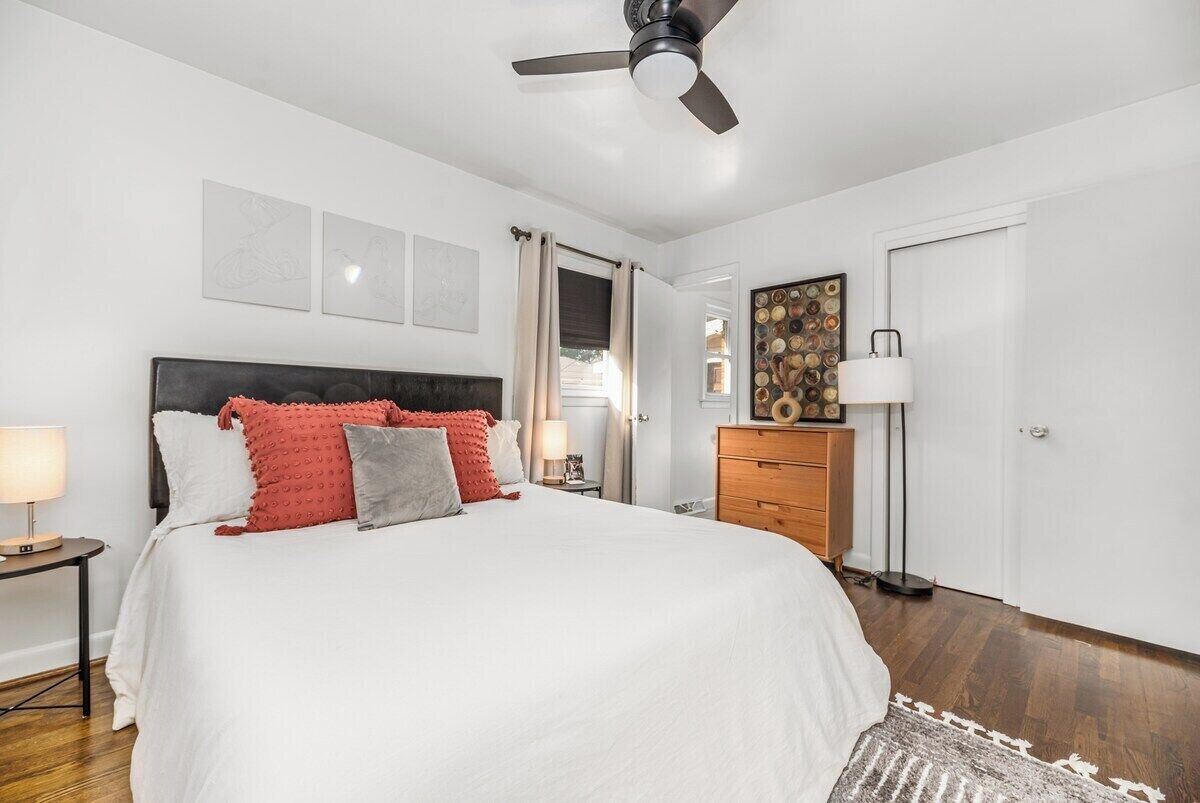 A bedroom with a bed, a ceiling fan, a nightstand, a dresser, and a door.