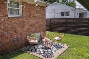A backyard with a brick wall, a wooden fence, and a patio area with wicker chairs and a patterned rug. - Renovated 3BR House - Monthly Stays - Fenced Quarter-Acre Yard - Pets Welcome (Charlotte)