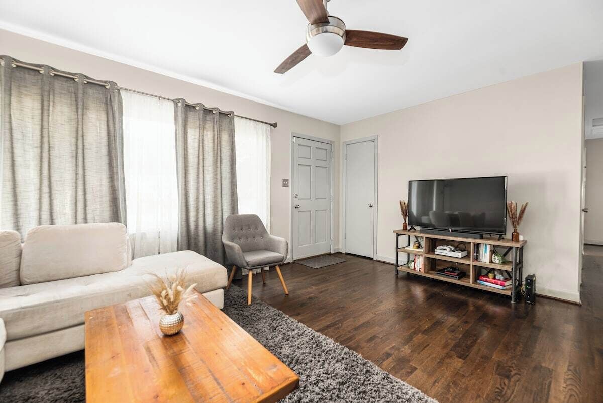 Ein Wohnzimmer mit Sofa, Sessel, Couchtisch, TV-Schrank und Deckenventilator.