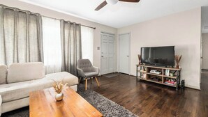 Una sala de estar con sofá, sillón, mesa de centro, mueble para televisión y ventilador de techo.