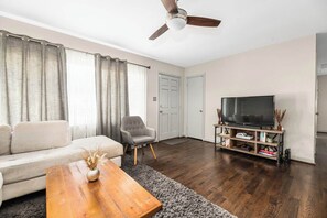 A living room with a sofa, armchair, coffee table, TV stand, and ceiling fan. - Renovated 3BR House - Monthly Stays - Fenced Quarter-Acre Yard - Pets Welcome (Charlotte)