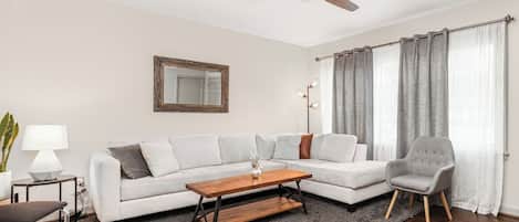 Un salon comprenant un canapé, une table basse, un fauteuil, un ventilateur de plafond, une lampe sur pied et un miroir au mur.