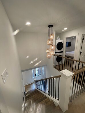 Una escalera con barandilla de madera y balaustradas negras que lleva a una habitación con lavadora y cama.