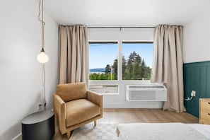 A room with a single brown chair, a bed, a standing heater, and a window with curtains. - New! Style & Harbor Views | Walk to Food & Tours (Juneau)