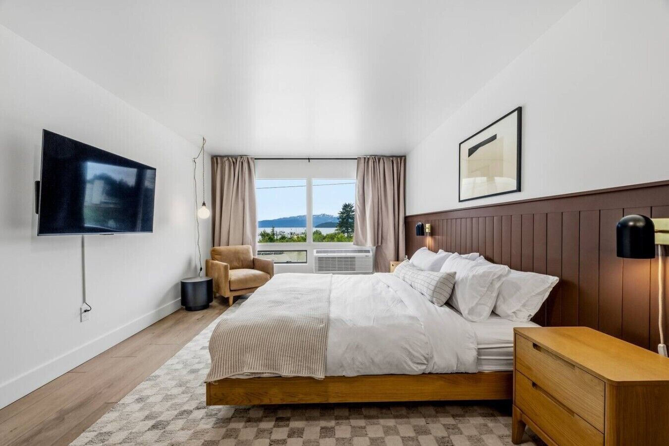 A modern hotel room with a bed, a TV, a chair, and a view of the outdoors.