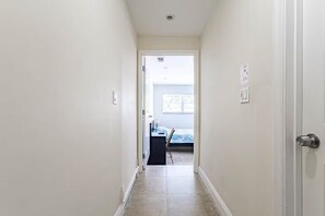 A narrow hallway with a door on the right, leading to a room with a bed and a desk. - Cozy 1-bedroom studio in soothing Virginia Gardens with AC (Virginia Gardens)