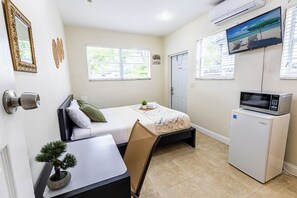 Een kleine hotelkamer met een bed, een bureau, een stoel, een kleine koelkast en een televisie.