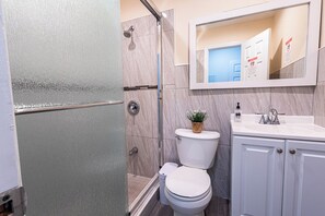 Een badkamer met een douche, toilet, wastafel en een spiegel boven de wastafel.
