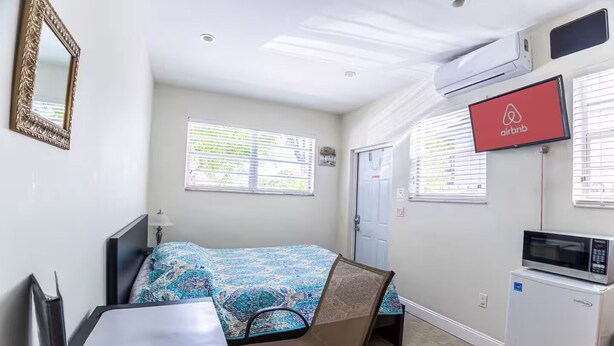 Ein kleines Hotelzimmer mit Bett, Schreibtisch, Stuhl, Fernseher und Kühlschrank.