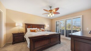 A bedroom with a large bed, two bedside tables with lamps, a ceiling fan, and a view through a sliding glass door. - Bright Golf View Villa: Vaulted Ceilings, Patio Dining, Mtn Views & Resort Pool (Palm Desert)