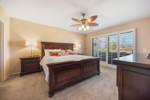 A bedroom with a large bed, two bedside tables with lamps, a ceiling fan, and a view through a sliding glass door. - Bright Golf View Villa: Vaulted Ceilings, Patio Dining, Mtn Views & Resort Pool (Palm Desert)