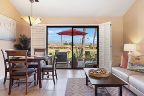 Ein Wohnzimmer mit Essbereich, einer Couch, einem Couchtisch und Blick auf einen Golfplatz durch eine Schiebetür.