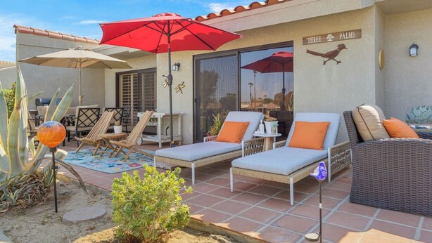 A patio area with lounge chairs, a red umbrella, and a sign reading 'Three Palms'. - Bright Golf View Villa: Vaulted Ceilings, Patio Dining, Mtn Views & Resort Pool (Palm Desert)