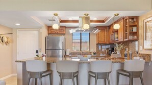 A modern kitchen with a central island, bar stools, stainless steel appliances, and wooden cabinetry. - Bright Golf View Villa: Vaulted Ceilings, Patio Dining, Mtn Views & Resort Pool (Palm Desert)