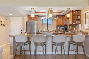 A modern kitchen with a central island, bar stools, stainless steel appliances, and wooden cabinetry. - Bright Golf View Villa: Vaulted Ceilings, Patio Dining, Mtn Views & Resort Pool (Palm Desert)