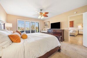 A hotel room with a large bed, a ceiling fan, a flat-screen TV, and a view of the outdoors through the window. - Bright Golf View Villa: Vaulted Ceilings, Patio Dining, Mtn Views & Resort Pool (Palm Desert)