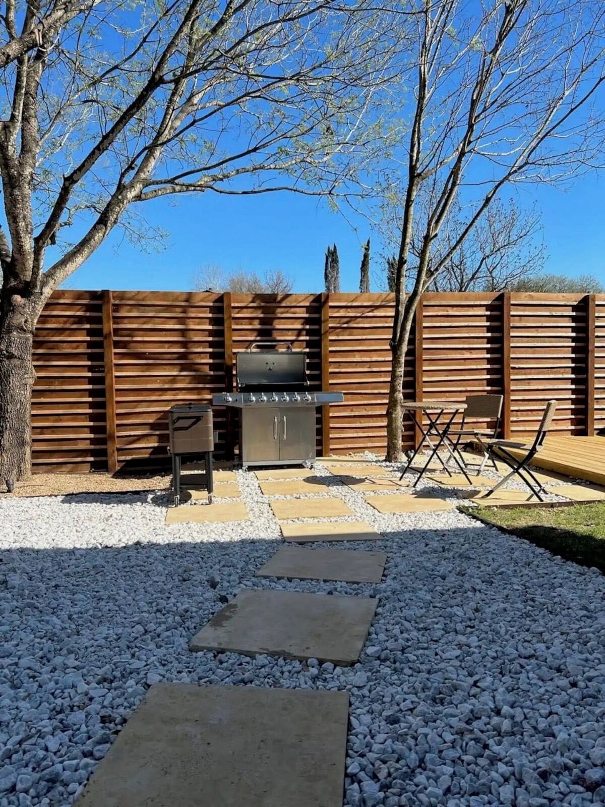 A backyard with a barbecue grill, a seating area with chairs, and a wooden fence.