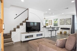 Ein modernes Wohnzimmer mit Flachbildfernseher, einer Treppe, einem Essbereich mit Barhocker und Kunstwerken an den Wänden.
