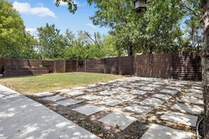 Ein Garten mit einer gepflasterten Terrasse, einem Holzzaun und Bäumen.