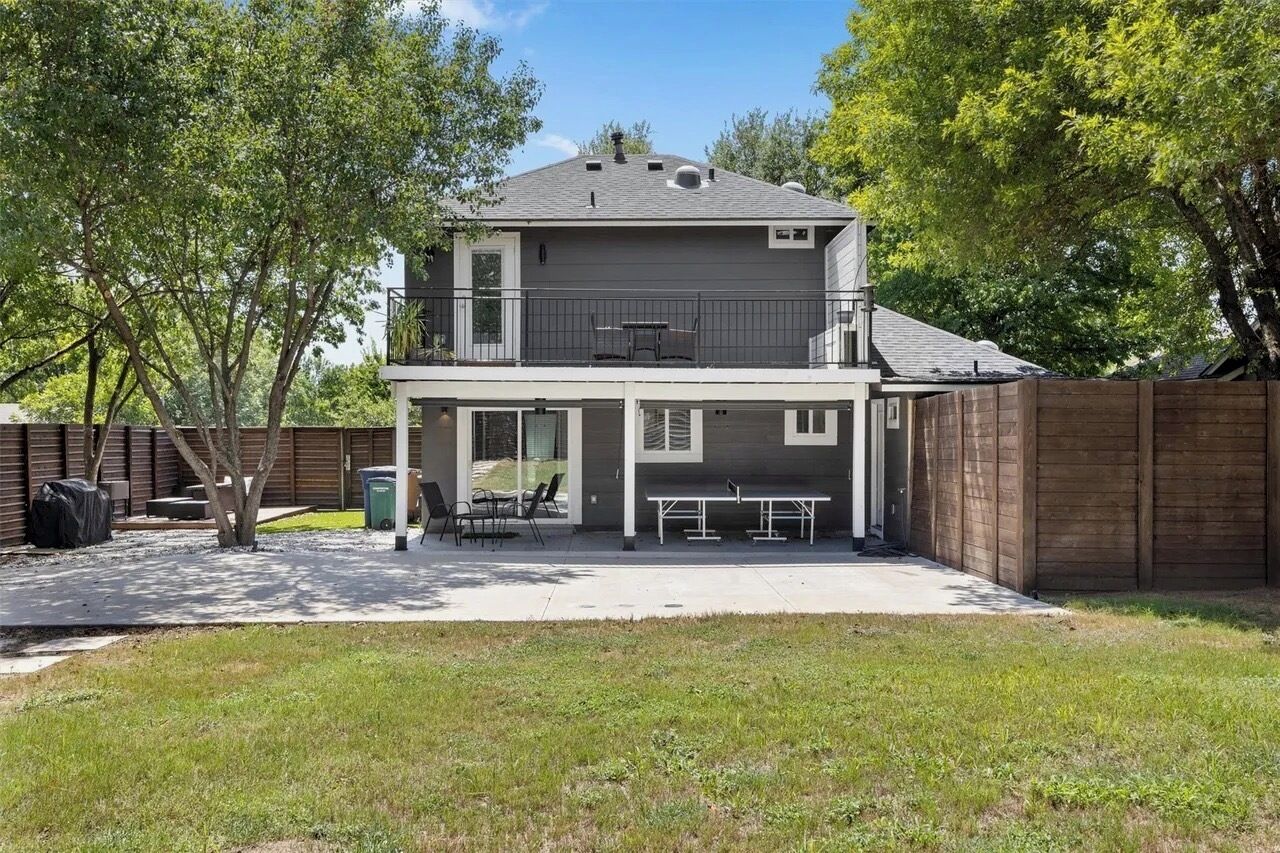 A two-story house with a covered patio area, a fenced backyard, and a tree in the foreground.