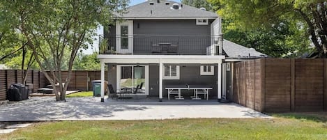A two-story house with a covered patio area, a fenced backyard, and a tree in the foreground.
