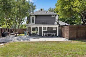 A two-story house with a covered patio area, a fenced backyard, and a tree in the foreground. - Spacious 4-bedroom home in South Austin with a private enclosed backyard space (Austin)