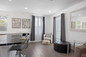 Ein modernes Wohnzimmer mit einem Glastisch, einem weißen Sessel, einem schwarzen Hocker und einem großen Spiegel an der Wand.