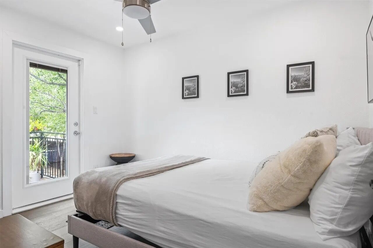 A bedroom with a bed, a ceiling fan, a door to a balcony, and three framed pictures on the wall.