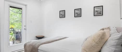A bedroom with a bed, a ceiling fan, a door to a balcony, and three framed pictures on the wall.
