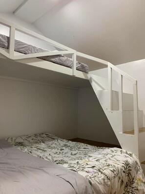 A bunk bed with a ladder, a lower bed with a floral bedspread, and a white ceiling.